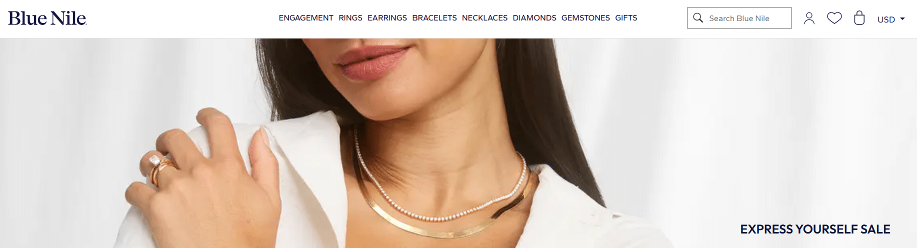 Model wearing elegant gold and diamond jewelry from Blue Nile, featuring rings and layered necklaces